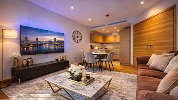 A modern living room with a flat-screen TV, a dining area, and a kitchen.