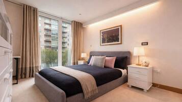 A hotel room with a large bed, bedside tables, a window with curtains, and a painting on the wall.