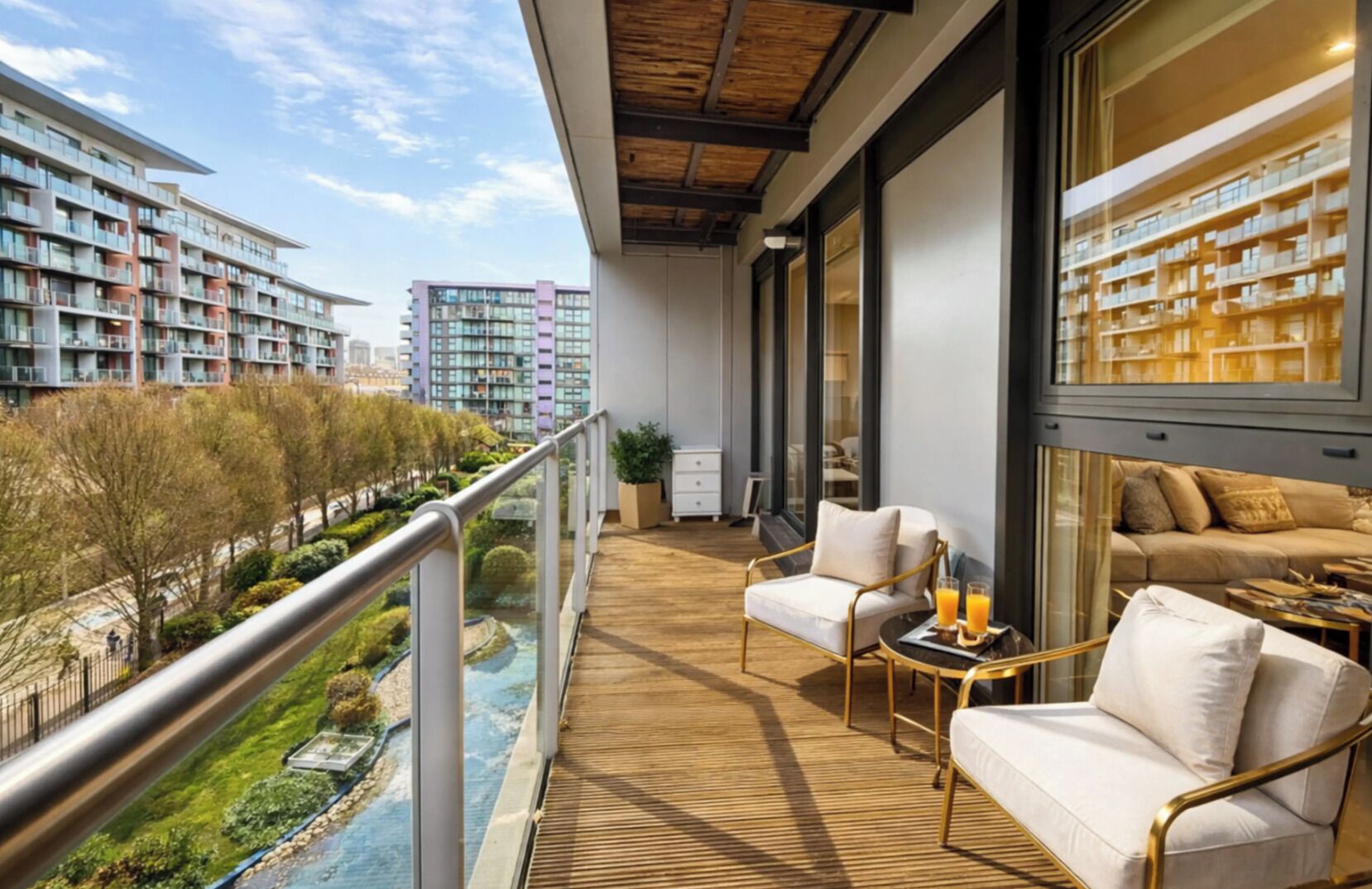 Een balkon met een houten vloer, een bank, een stoel en een tafel met een tray sinaasappelsap.