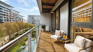 A balcony with a wooden floor, a sofa, a chair, and a table with a tray of orange juice.