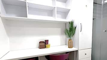 A compact room with a white desk, a purple chair, a small plant, and a wardrobe.