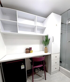 Ein kompakter Raum mit einem weißen Schreibtisch, einem violetten Stuhl, einer kleinen Pflanze und einem Kleiderschrank.
