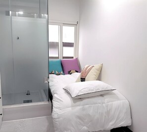 Ein Schlafzimmer mit Bett, Fenster und Duschbereich.