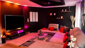 A modern living room with a flat-screen TV, a sofa, a coffee table, and a decorative vase with flowers. - Must-See / Jacuzzi - Pool - Sauna - Turkish Bath (Challans)