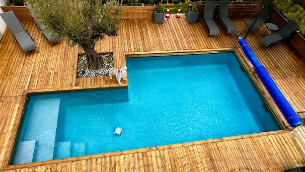 A rectangular swimming pool with a wooden deck surrounding it, a tree, and lounge chairs. - Must-See / Jacuzzi - Pool - Sauna - Turkish Bath (Challans)