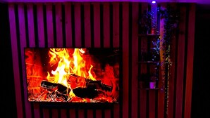 A room with a heated floor, a television displaying a fire, and a hot tub with illuminated controls. - Must-See / Jacuzzi - Pool - Sauna - Turkish Bath (Challans)