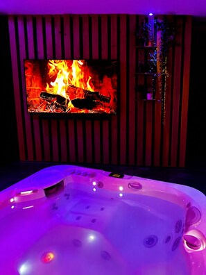 Ein Zimmer mit warmer Fußbodenheizung, einem Fernseher, der ein Feuer zeigt, und einer Whirlwanne mit beleuchteten Bedienelementen.