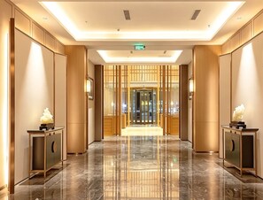 A hotel lobby with a marble floor, wooden paneling, and a reception desk.