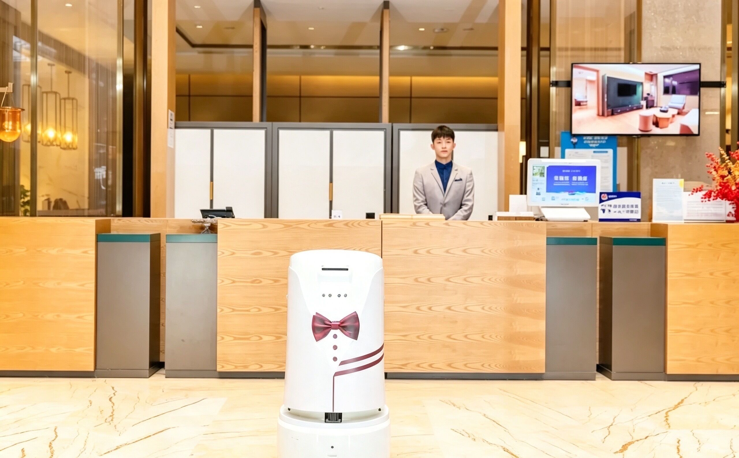 A hotel reception desk with a digital screen, a receptionist, and a decorative item resembling a bow tie on a cylindrical object.