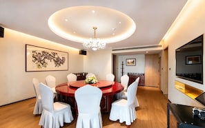 A dining area with a round table, white chairs, a chandelier, and artwork on the walls.