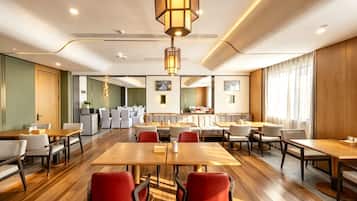 A hotel dining area with multiple tables and chairs, a central light fixture, and a view of the adjacent room.