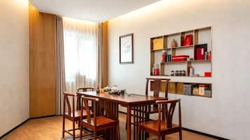 A dining area with a wooden table and chairs, a bookshelf with various items, and a window with curtains.