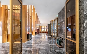 A hotel corridor with a marble floor, wooden paneling, and glass doors leading to rooms.