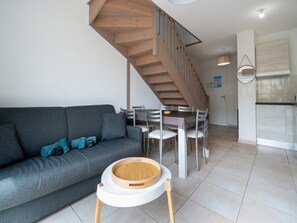 A modern living room with a grey sofa, a dining table, and a staircase leading to an upper level. - Seaside Comfort in Valras (Sérignan)