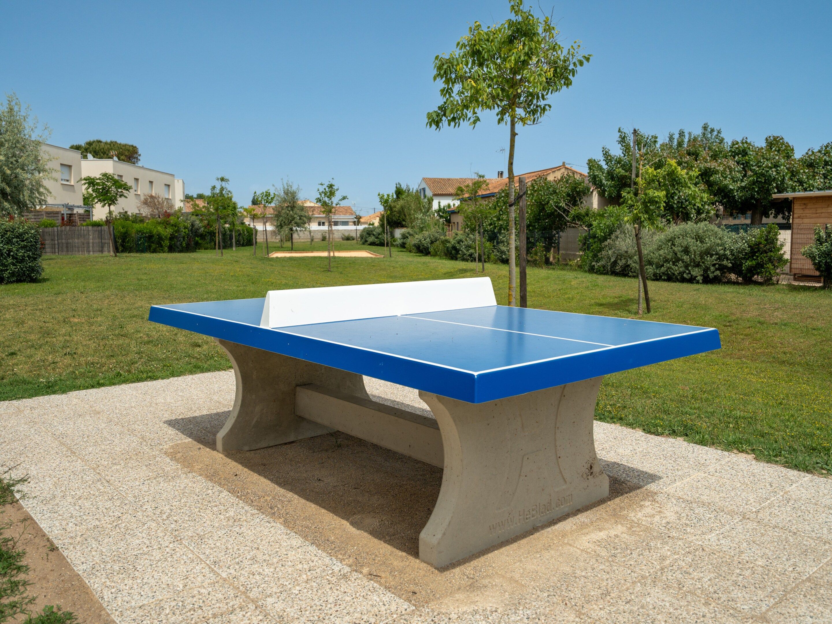 A concrete ping pong table in a park with a clear sky.