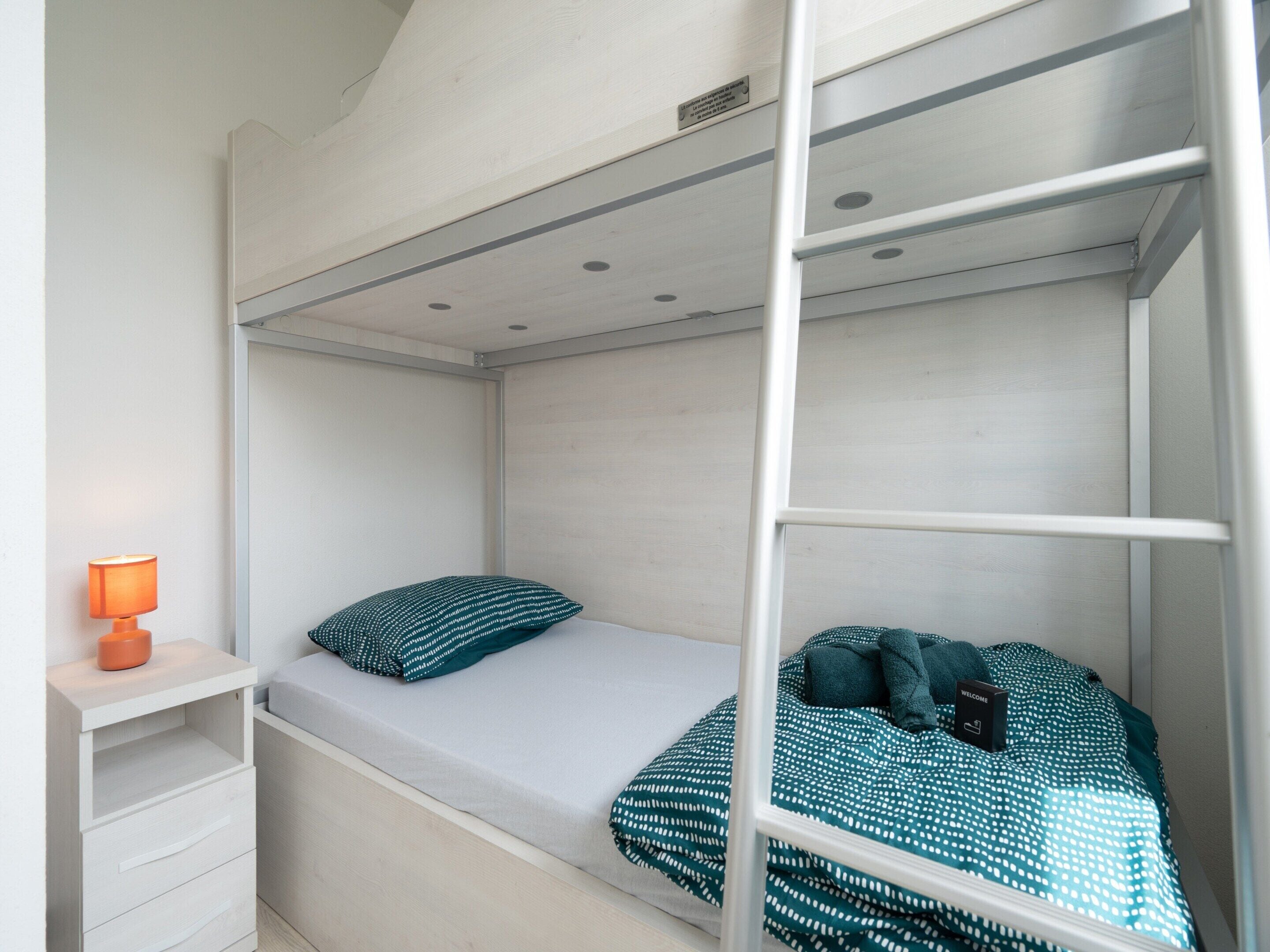 A bunk bed with a single bed on the lower bunk and a nightstand with a lamp.
