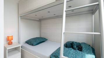 A bunk bed with a single bed on the lower bunk and a nightstand with a lamp.