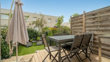 An outdoor patio with a table and chairs, a wooden deck, and a fence.