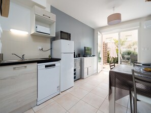 A modern kitchen with a dishwasher, refrigerator, microwave, and a dining area with a table and chairs. - Seaside Comfort in Valras (Sérignan)