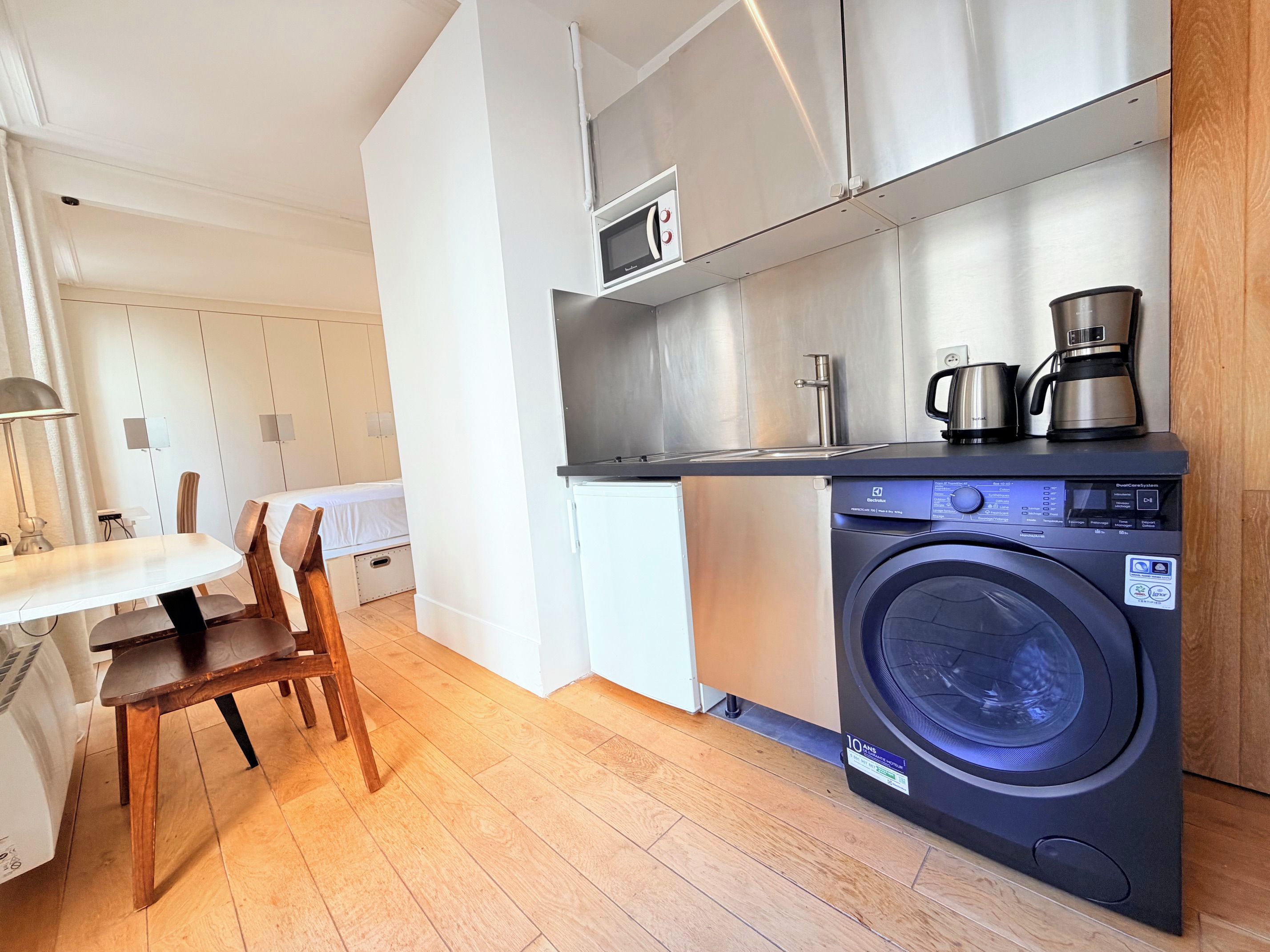 A compact kitchen with a washing machine, a coffee maker, and a microwave.