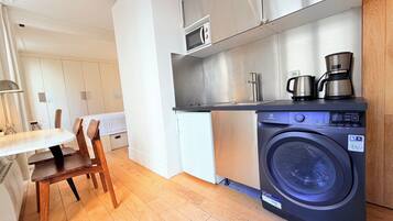 A compact kitchen with a washing machine, a coffee maker, and a microwave.