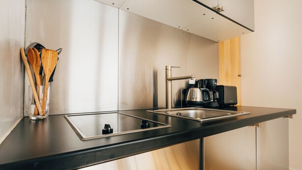Una cocina moderna con cubierta negra, pileta de acero inoxidable y cafetera.