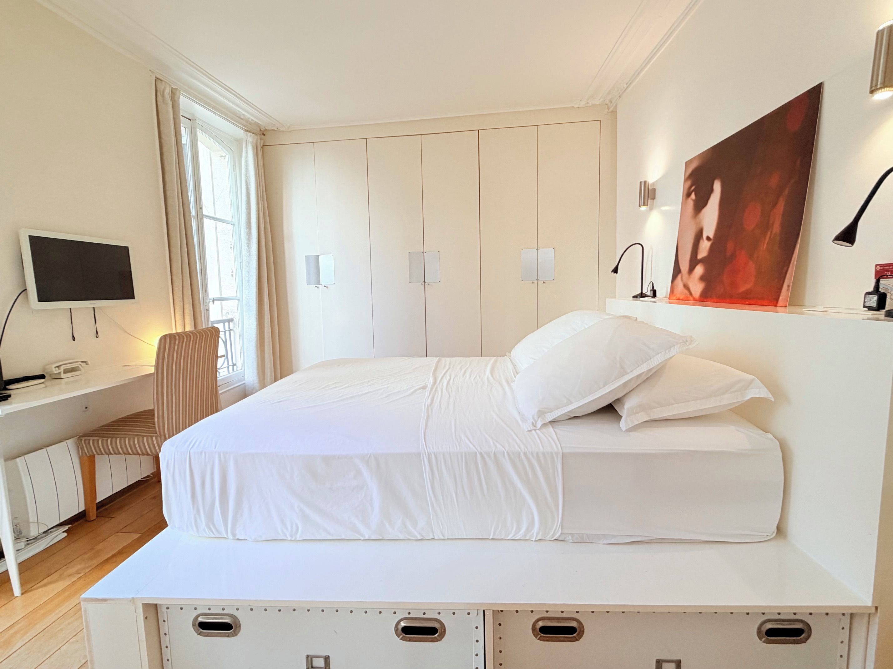 Une chambre d’hôtel avec un lit, un bureau, une chaise, une télévision et une fenêtre avec des rideaux.