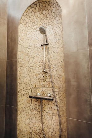 Ducha con pared de diseño de piedra y cabezal de ducha cromado.