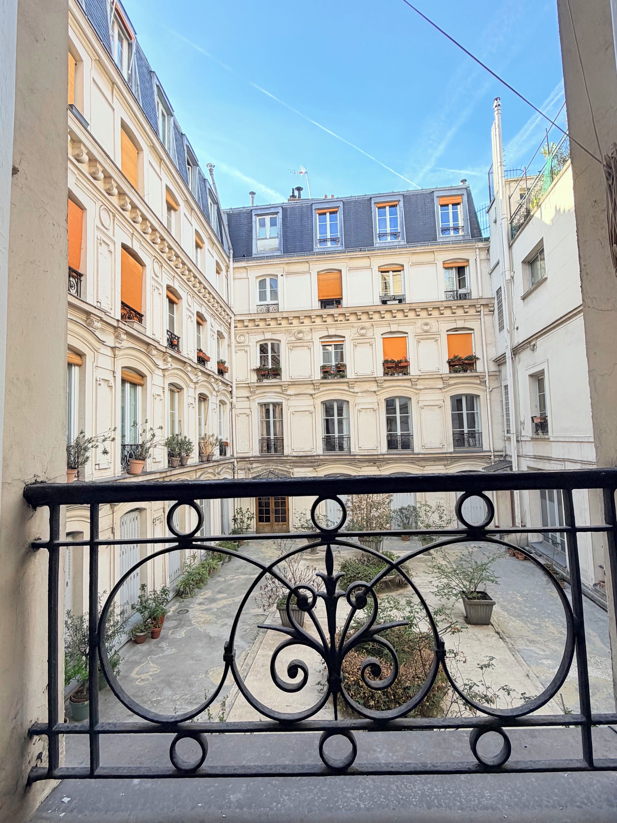 A courtyard with buildings on either side, featuring balconies with potted plants.