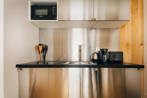 Eine kompakte Küche mit Edelstahl-Spüle, Kaffeemaschine und Mikrowelle.
