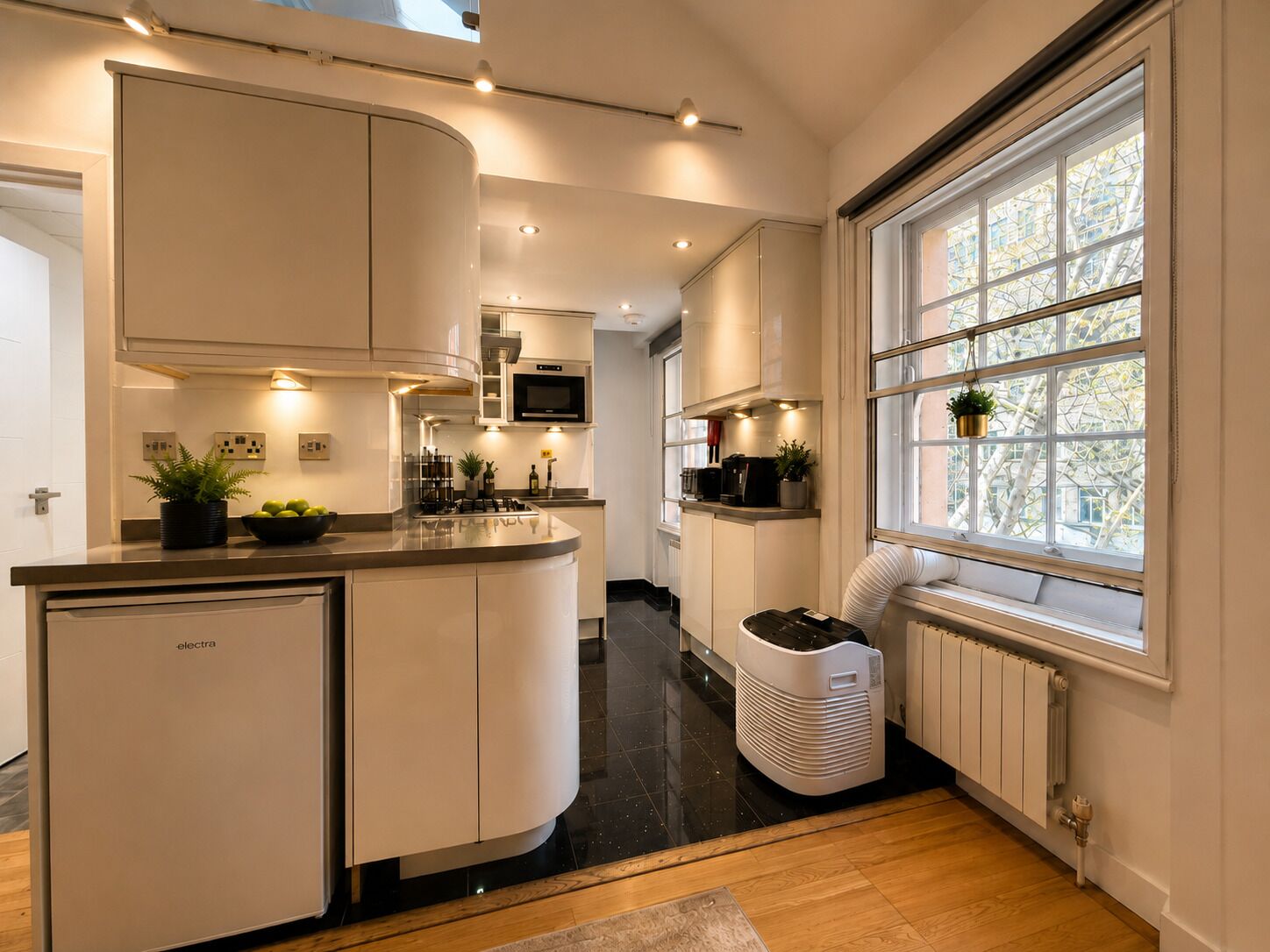 Une cuisine moderne dotée d’un îlot central aux lignes courbes, d’appareils électroménagers intégrés et d’une fenêtre offrant une vue agréable.