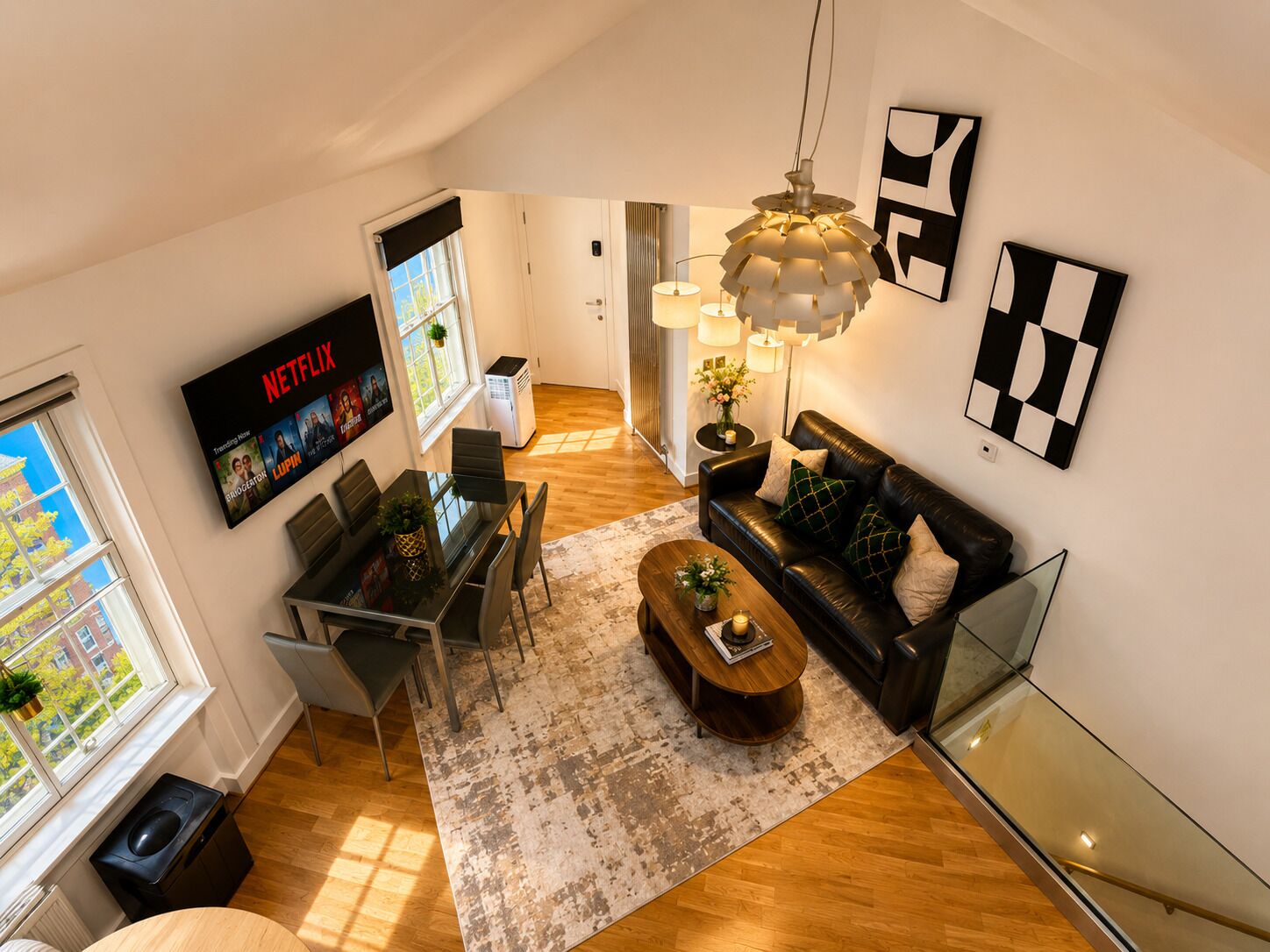 Un salon moderne avec un canapé en cuir noir, une table basse, un coin repas doté d’une table en verre et un téléviseur fixé au mur.