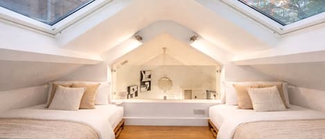 A bedroom with two beds, a skylight, and a view of the city.
