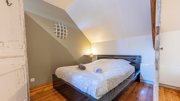 Un dormitorio con una cama, una lámpara de pared y suelo de madera.