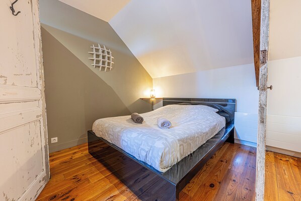 A bedroom with a bed, a wall-mounted light, and a wooden floor.
