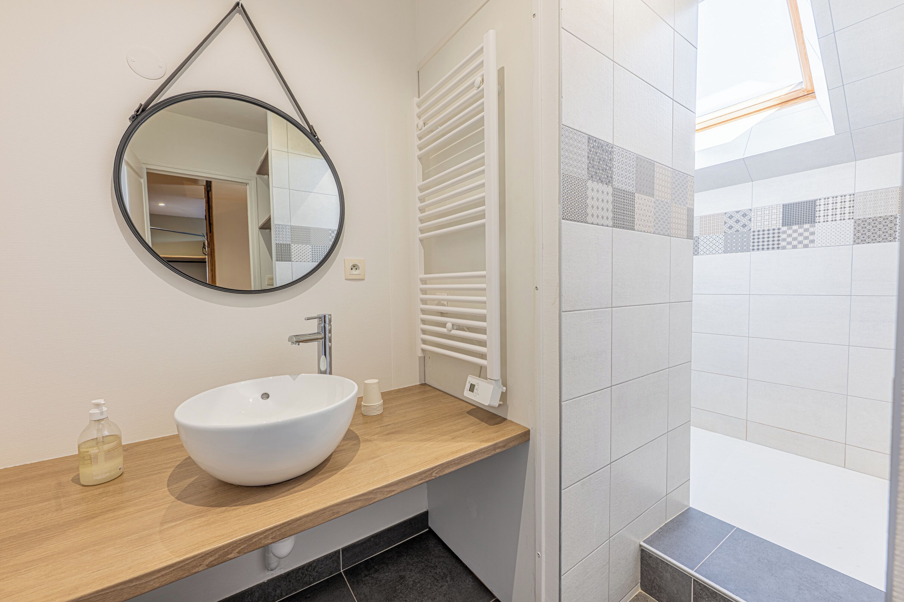 Une salle de bain moderne avec un miroir rond, un lavabo blanc et un espace douche.