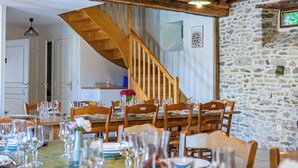 Un comedor con mesas y sillas de madera, una pared de piedra y una escalera de madera.