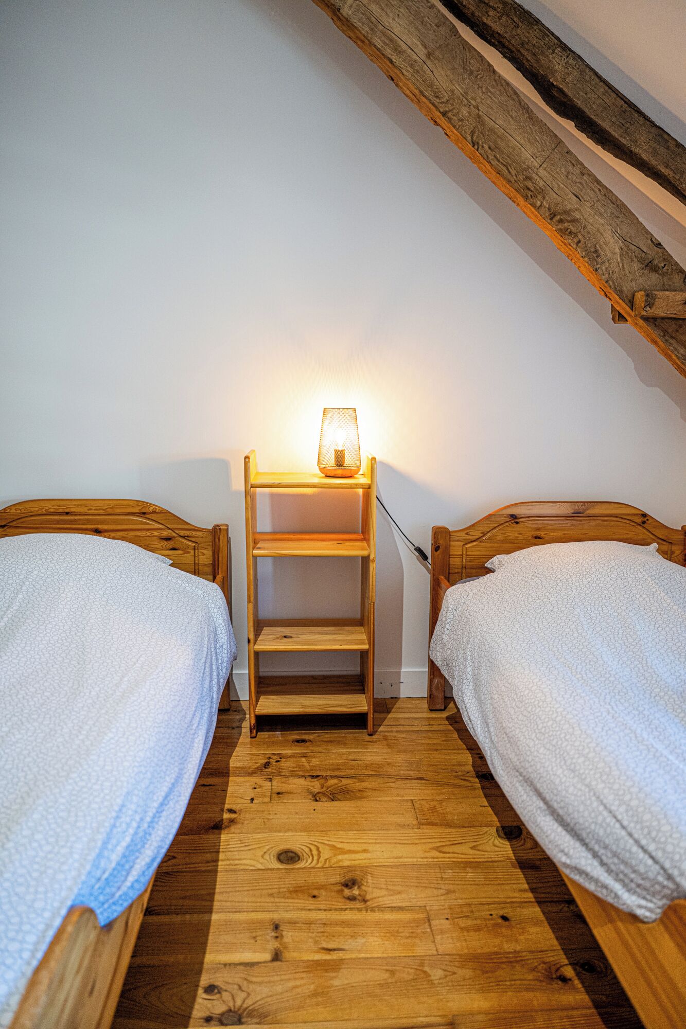 Una stanza accogliente e piccola con due letti di legno, una mensola di legno con una lampada e un soffitto spiovente.