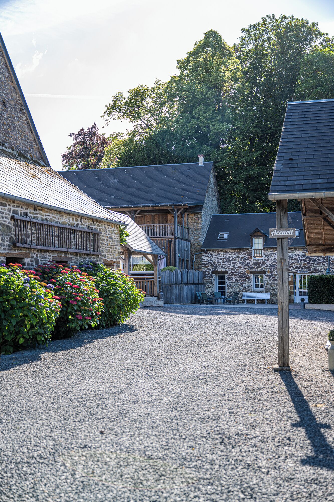 Une cour bordée de bâtiments en pierre, avec une clôture en bois et un chemin de gravier.