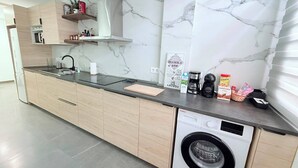 A modern kitchen with a built-in washing machine, marble backsplash, and wooden cabinetry. - Caletillas BlackSand—ocean views—Wi-Fi—garage—2 bedrooms, pool. (Candelaria)