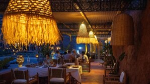 Un área de comedor al aire libre con mesas y sillas, iluminación colgante y vista al mar.