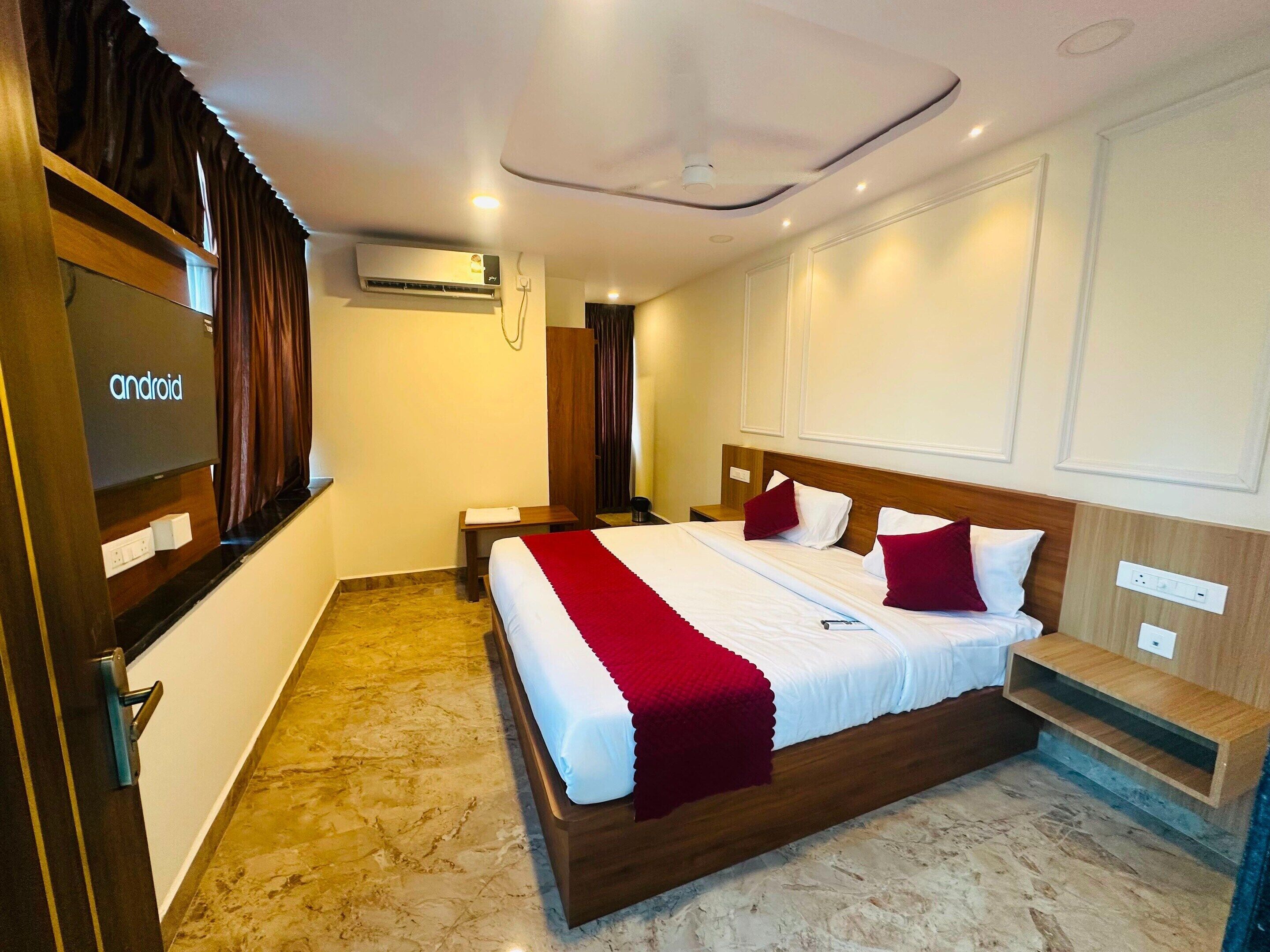 A hotel room with a bed, bedside tables, an air conditioning unit, and a television.