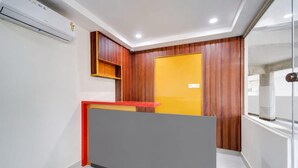 A reception area with a modern design, featuring a reception desk, a wooden panel wall, and a glass door. - Classic Aditya Grand Inn (Guntur)