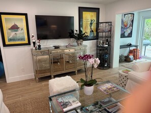 Ein Wohnzimmer mit einem Glastisch, einem weißen Sofa, einem Fernseher und einem Bücherregal.