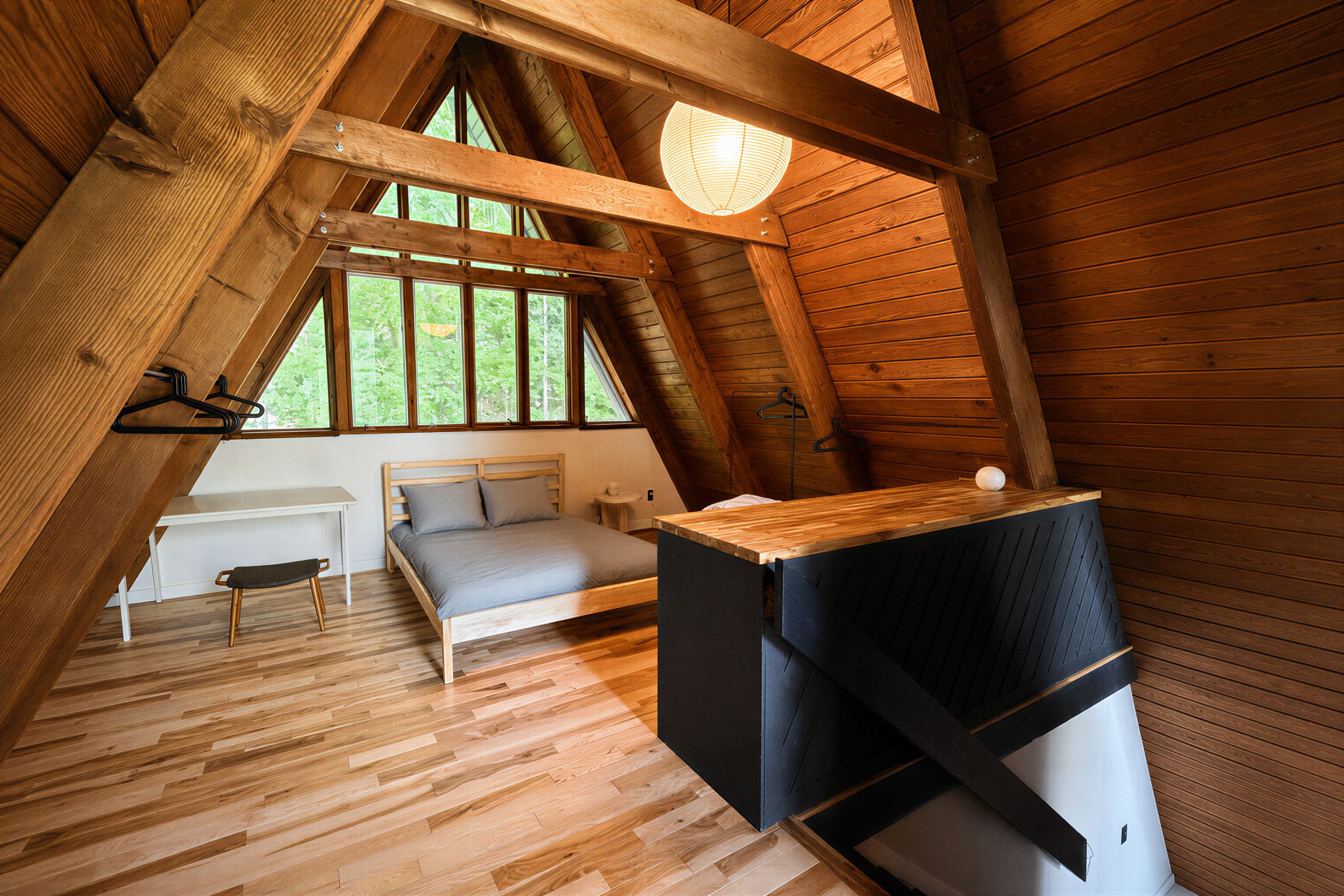 A loft-style bedroom with a sloped ceiling, a bed, a small table, and a hanging light fixture.