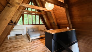 A loft-style bedroom with a sloped ceiling, a bed, a small table, and a hanging light fixture.