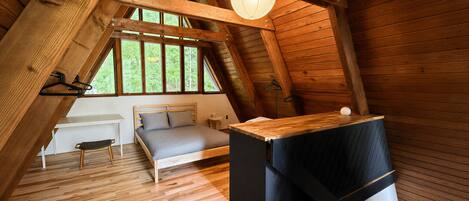 Ein Schlafzimmer im Loft-Stil mit schrägem Dach, einem Bett, einem kleinen Tisch und einer Pendelleuchte.