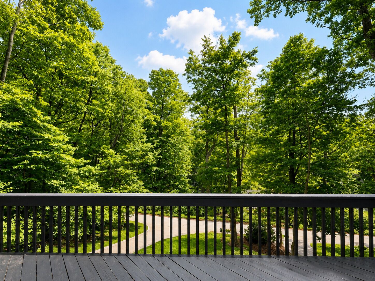 A wooden deck with a view of a winding road and dense green trees.