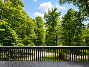 A wooden deck with a view of a winding road and dense green trees. - Custom A-Frame | Lake Access • Fire Pit (Highland Lakes)