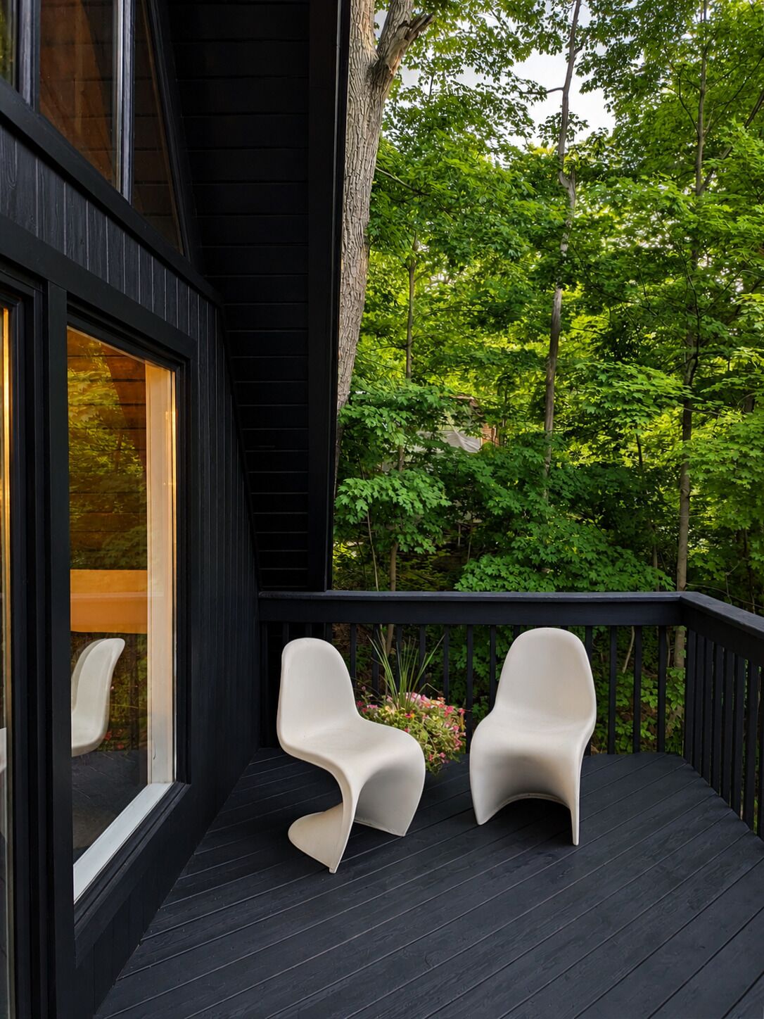 A deck with two modern chairs and a glass door leading to a room.